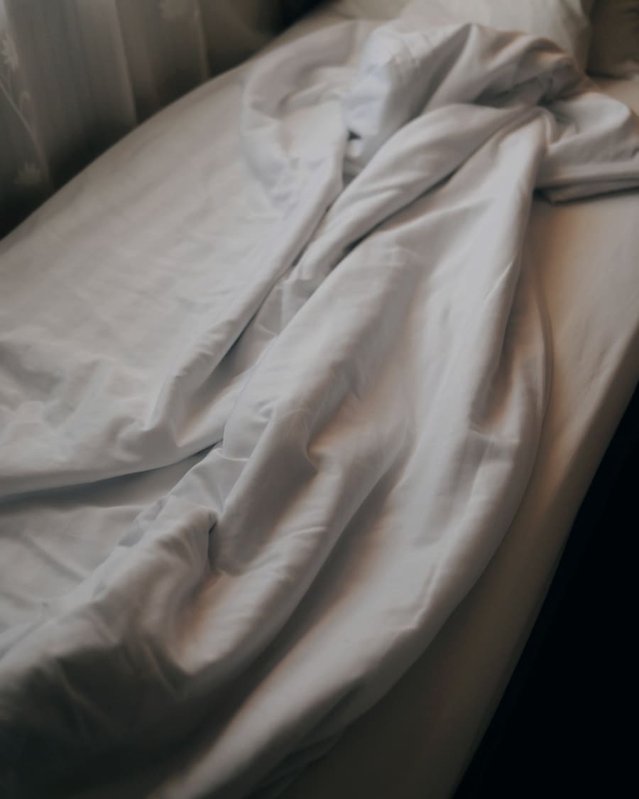 A bed with white sheets under a window, early light across it.