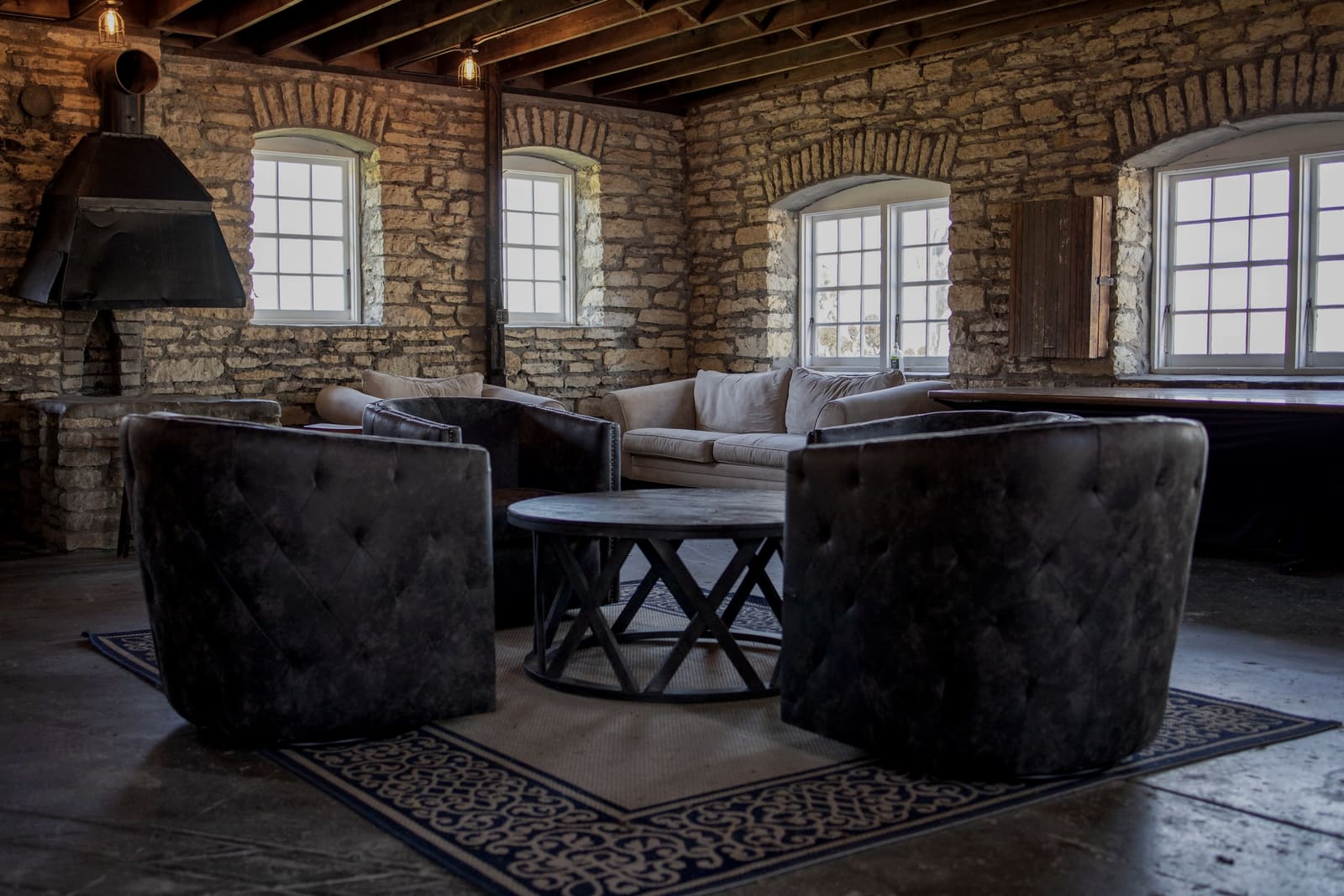 Sitting room with stone walls, beamed ceiling and a wood stove hood.